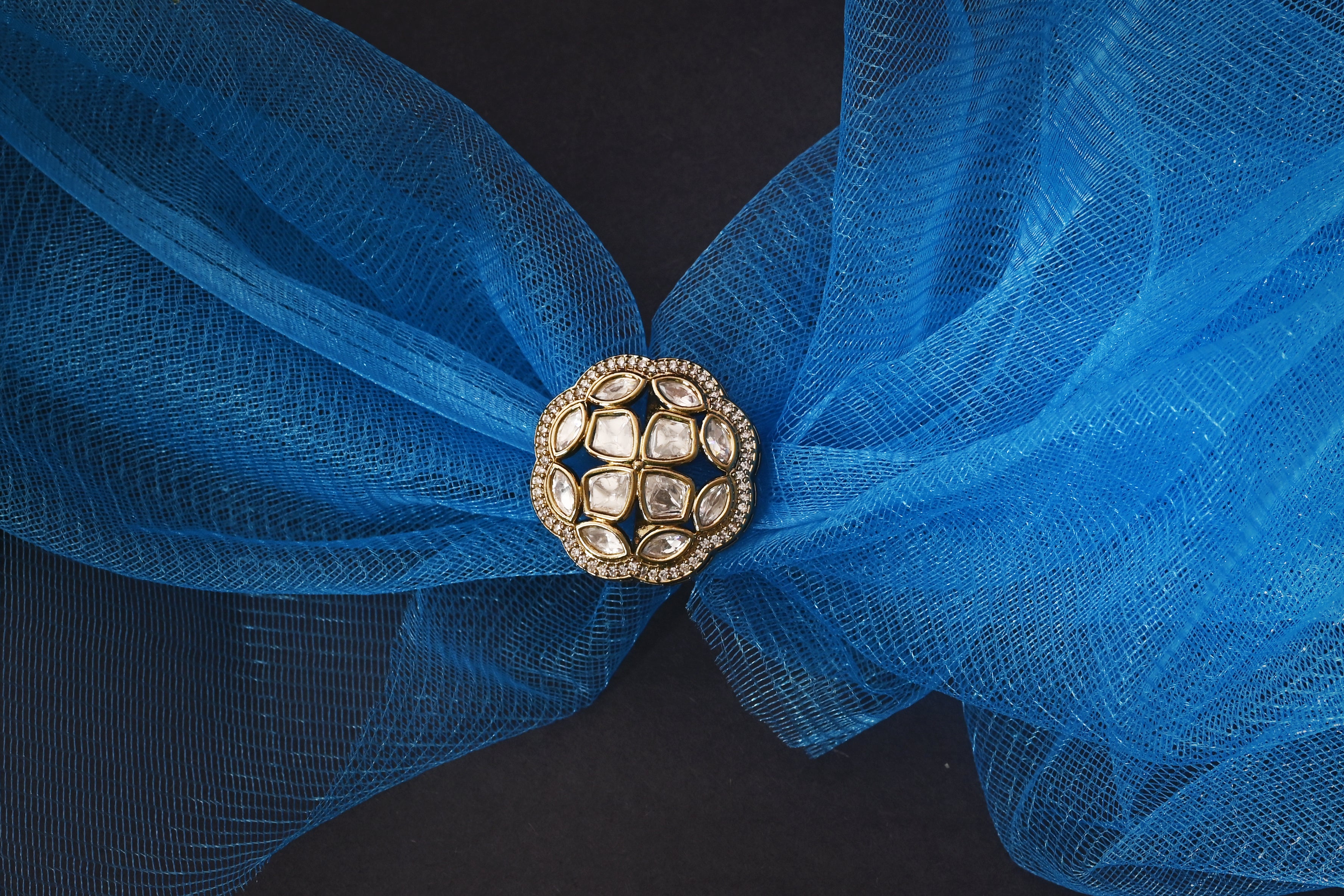 Blue fabric with a decorative gold brooch on a black background